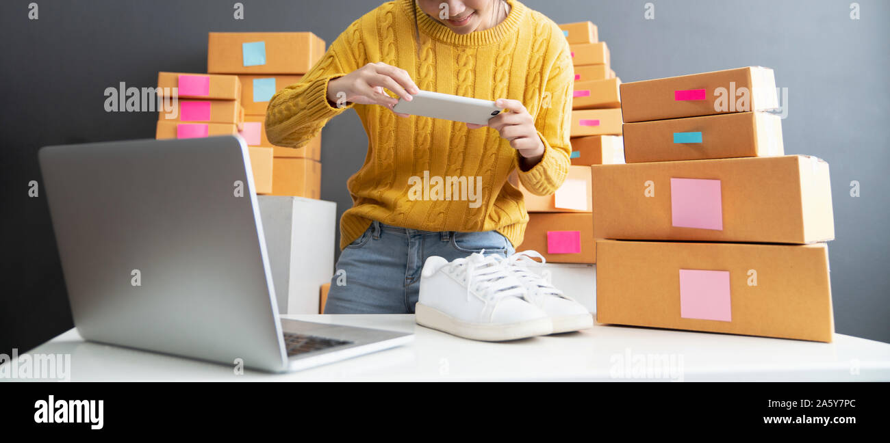Junge Frauen, die foto Schuhe mit Mobiltelefon oder Smartphone digitale Kamera für Post und online über das Internet zu verkaufen und Vorbereitung Pack Produkt Stockfoto