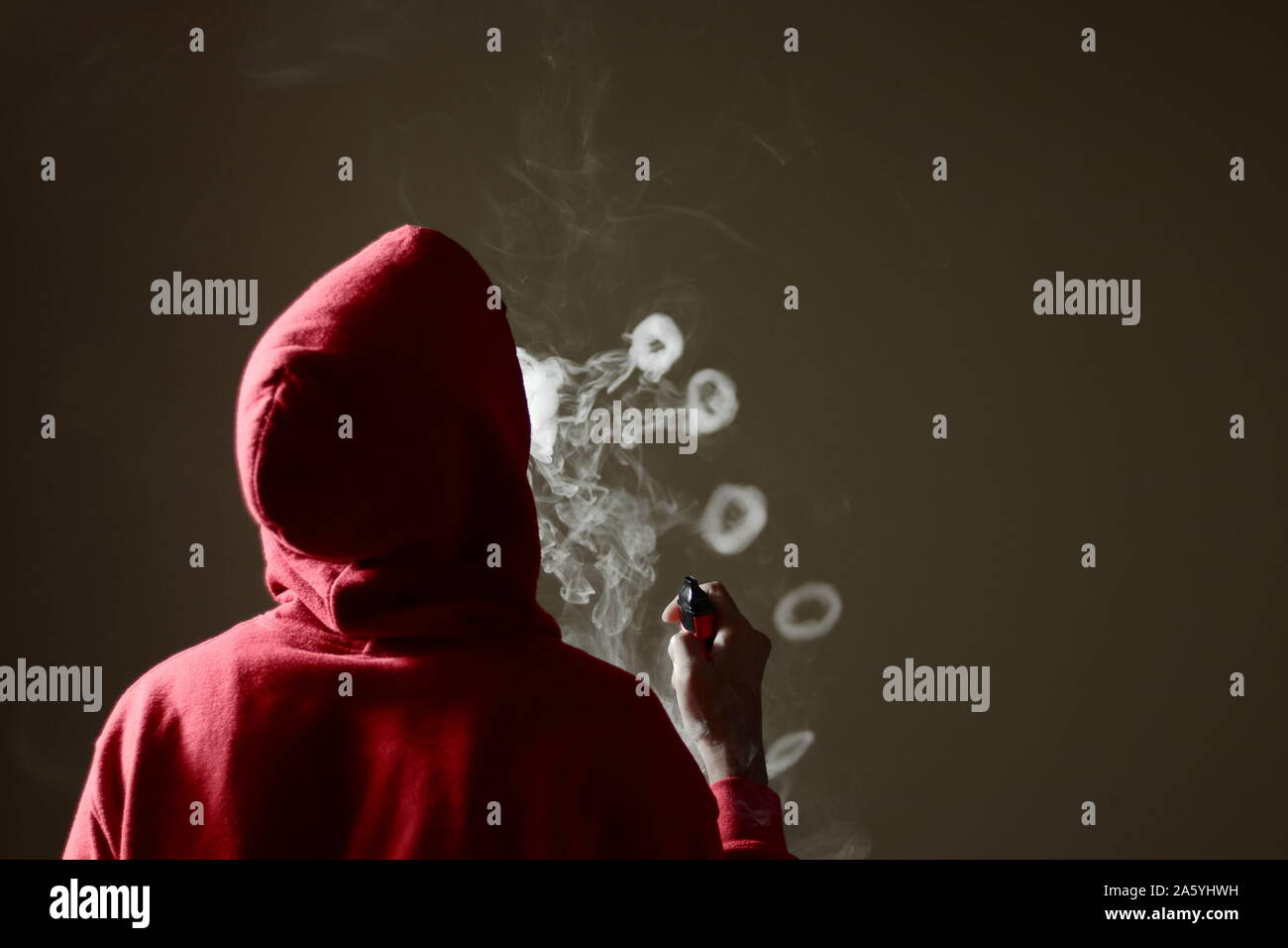 Junge Mann in Rot hoodie vaping Rauchen, bläst mehrere Rauch Ringe, während  eine vape in der Hand, isolierte Rückansicht Stockfotografie