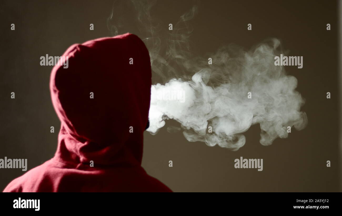 Junge Mann in Rot hoodie vaping Rauchen, atmet aus dicken Dampf, isolierte Rückansicht Stockfoto