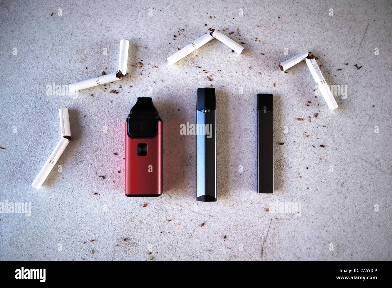 Verschiedene vape Geräte elektronische Zigaretten rauchen als Alternativen mit gebrochenen Zigaretten und Tabak verstreut auf Weiß strukturierten Hintergrund Stockfoto
