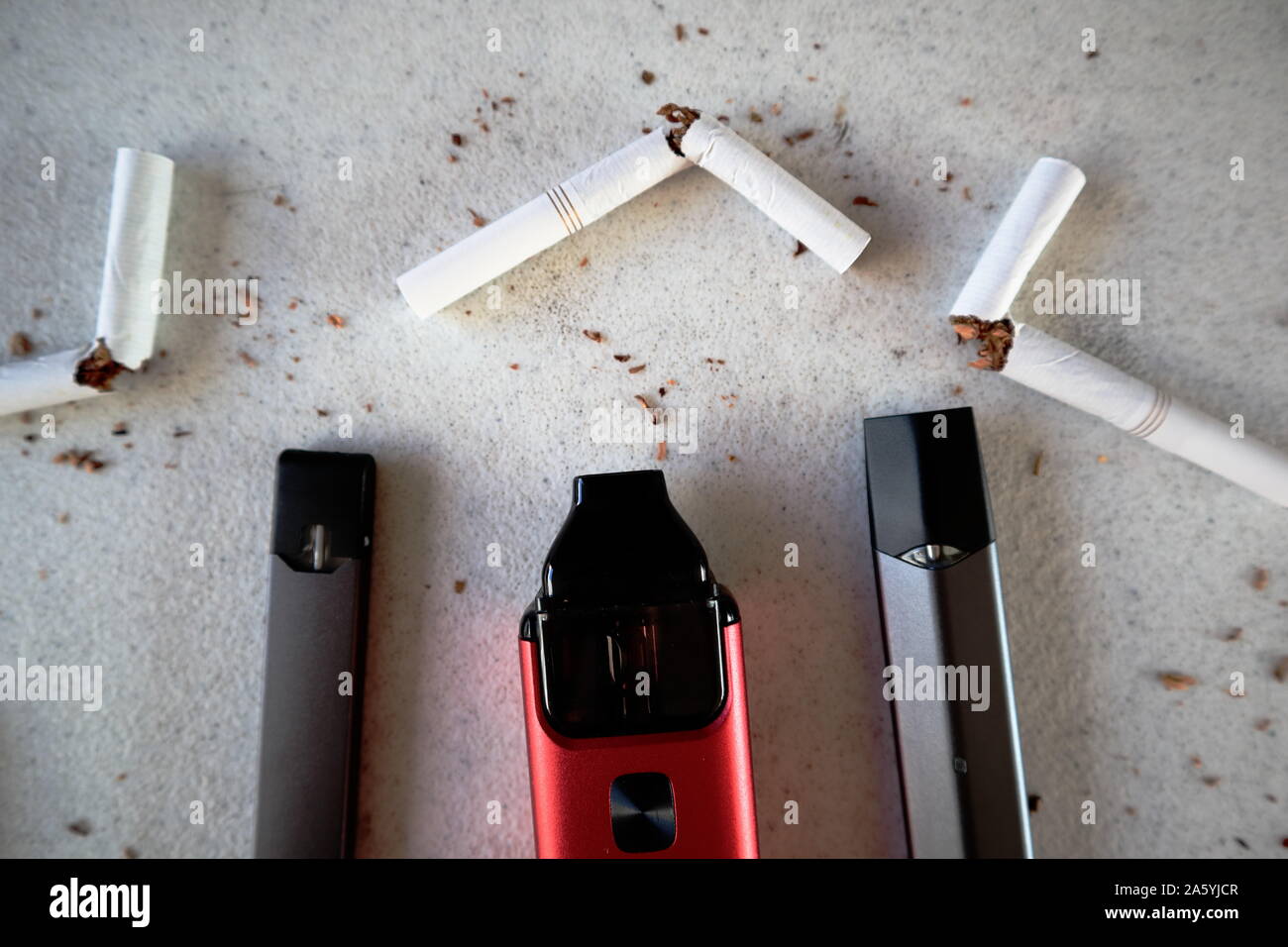 Verschiedene vape Geräte elektronische Zigaretten rauchen als Alternativen mit gebrochenen Zigaretten und Tabak verstreut auf weiße strukturierte Hintergrund schließen u Stockfoto