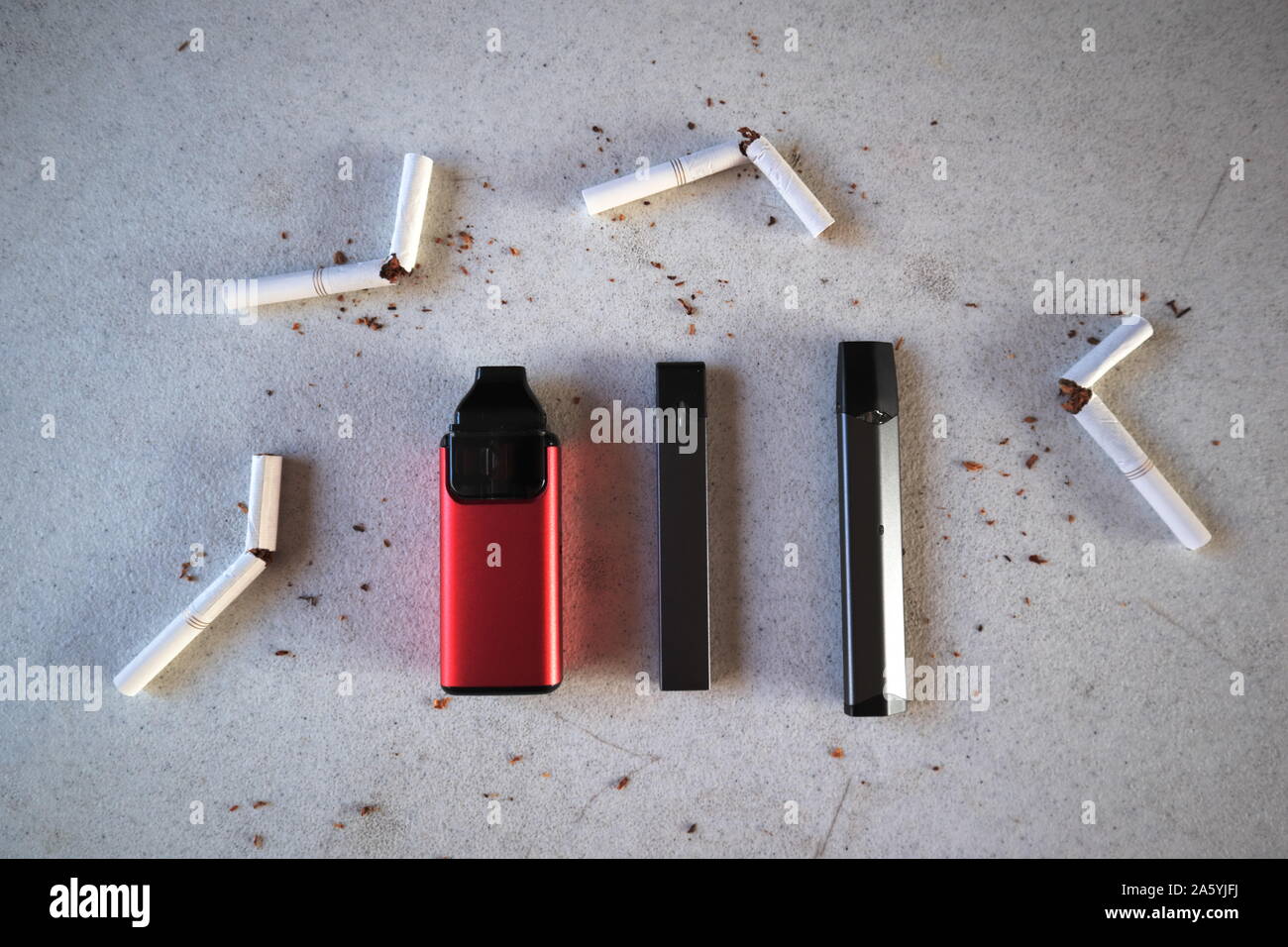 Verschiedene vape Geräte elektronische Zigaretten rauchen als Alternativen mit gebrochenen Zigaretten und Tabak verstreut auf Weiß strukturierten Hintergrund Stockfoto