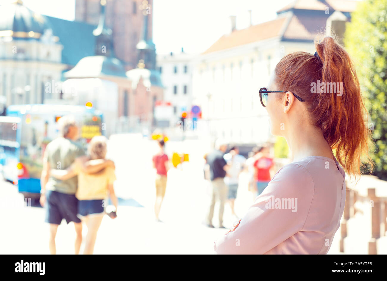 Eine junge Frau steht auf einer belebten Straße, vorbei an Menschen Stockfoto