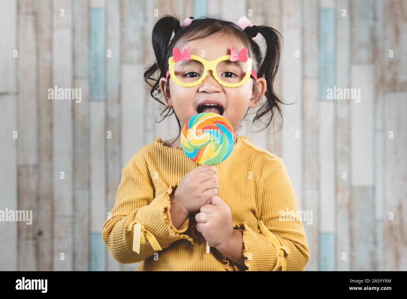 Süße kleine asiatische Mädchen halten und essen eine bunte Lollipop. Konzept der Mundpflege und Süßigkeiten Tag Stockfoto
