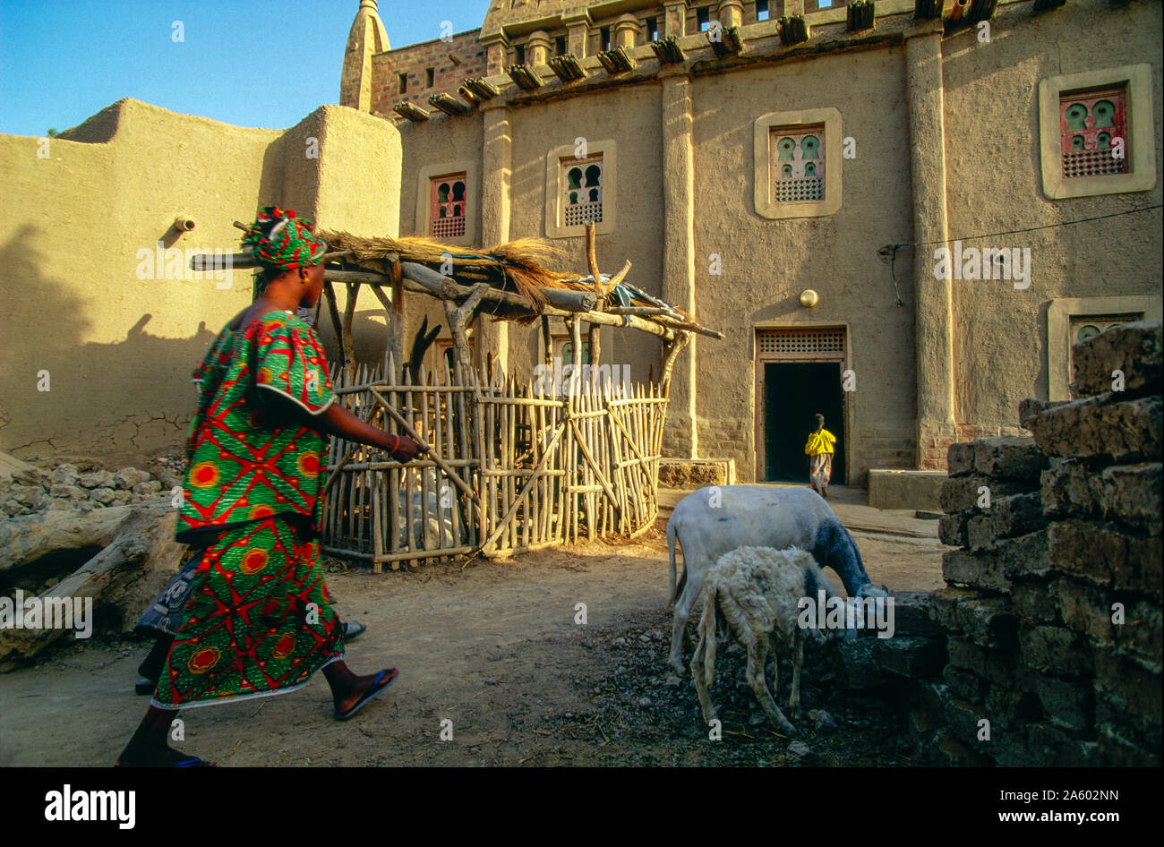 Djenne - Mali; eine Frau in traditioneller Kleidung an einem Haus mit schafstall in der marokkanischen Quartal. Stockfoto