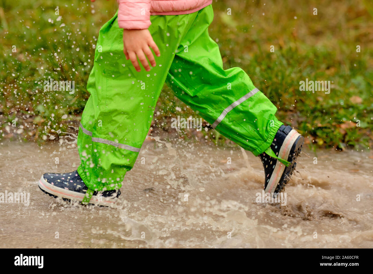 Seite angesichts der niedrigen Abschnitt eines Kindes Mädchen in Grün wasserdichte Hosen und Gummistiefel durch eine riesige regen Pfütze im Wald auf einem regnerischen Herbst Stockfoto