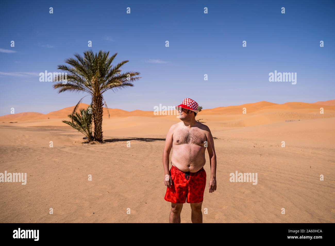 Übergewicht Mann mit Badeshorts und Hut steht in der Wüste von Marokko Stockfoto