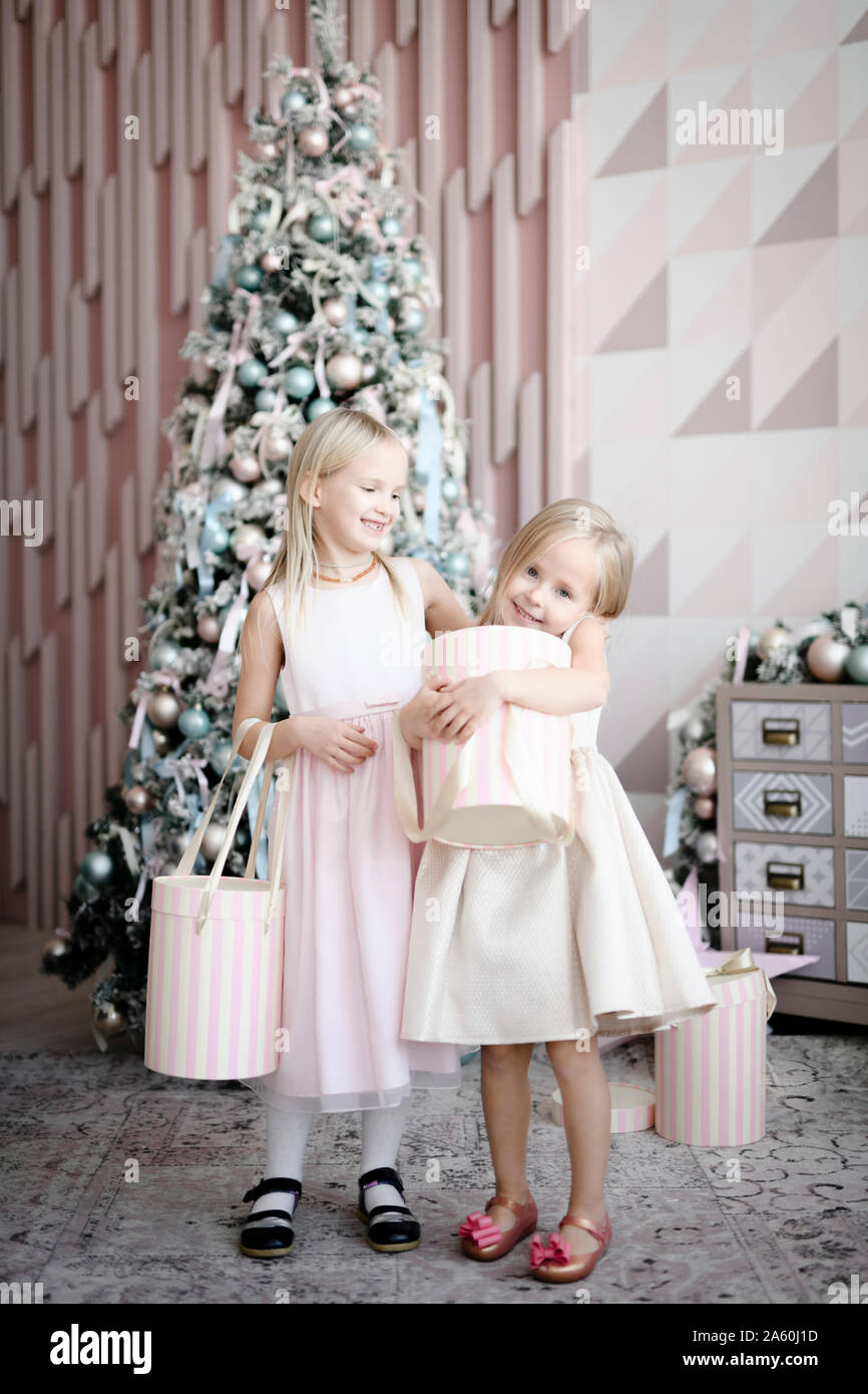 Porträt von zwei glücklichen kleinen Mädchen stand vor der beleuchteten Weihnachtsbaum mit Geschenkboxen Stockfoto