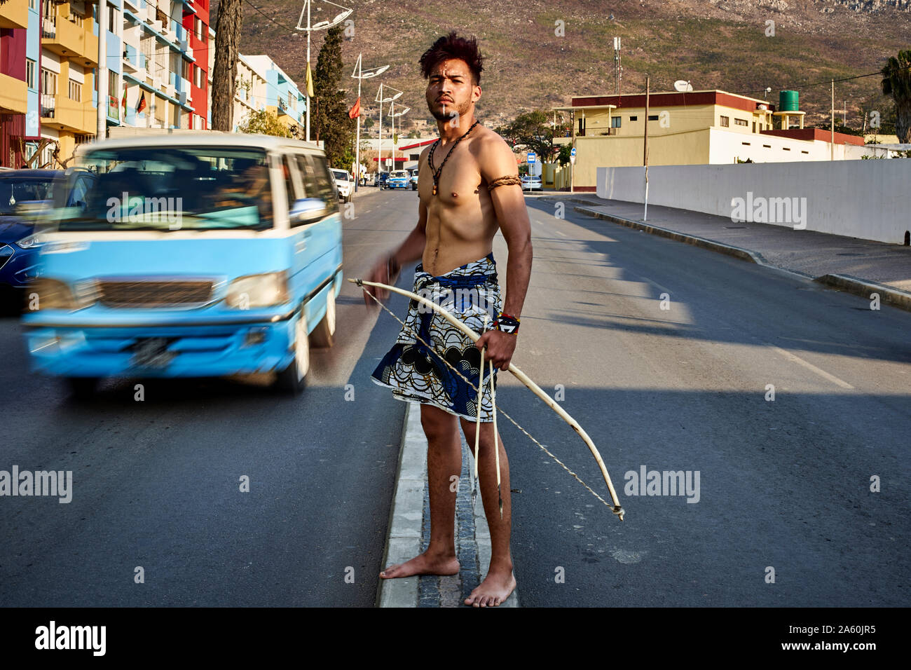 Tribal Mann mit seinem traditionellen Bogen und Pfeile in der Mitte der Stadt mit Autos vorbei, Lubango, Angola Stockfoto