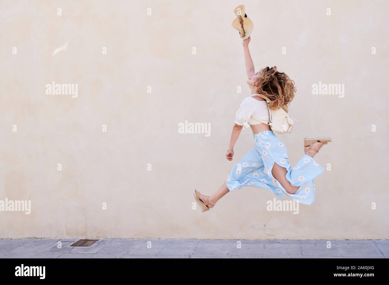 Unbeschwerte junge Frau mit Hut an einer Wand springen Stockfoto