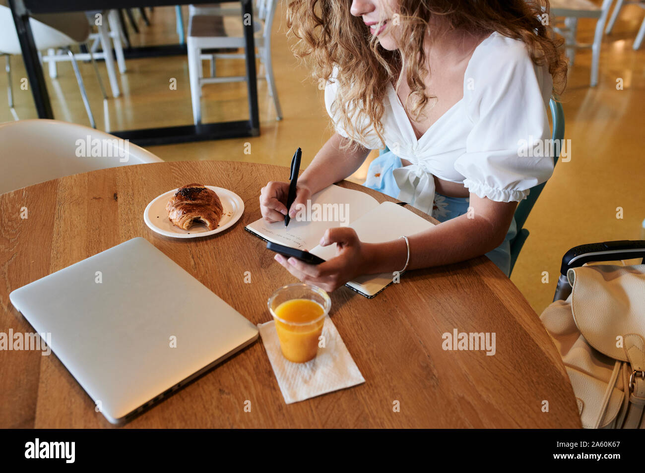 Junge Frau in einem Café mit Smartphone und Notizen beim Frühstück Stockfoto