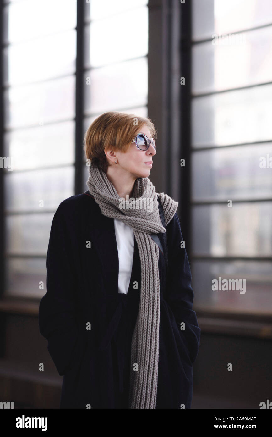 Reife Frau mit Sonnenbrille mit schwarzen Mantel und langen Wolle Schal an Plattform warten Stockfoto
