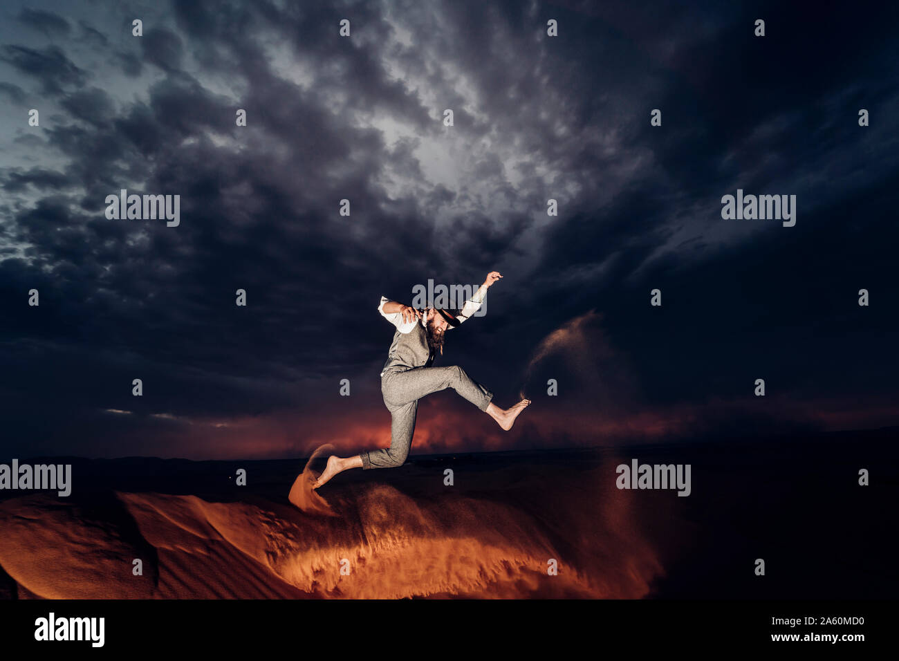 Mann mit Bart und Mütze springen in den Dünen der Wüste von Marokko in der Dämmerung Stockfoto