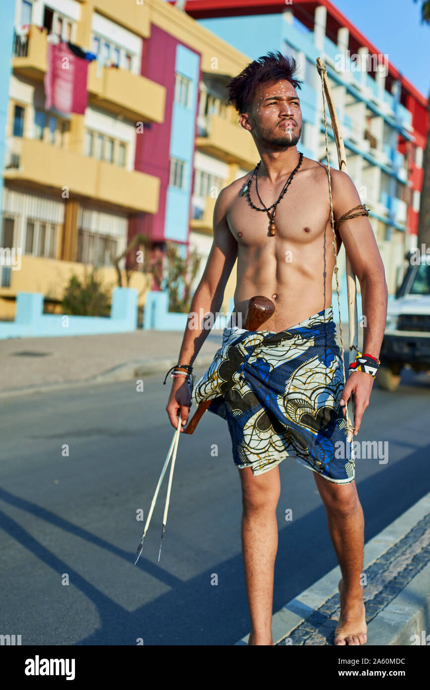 Tribal Mann mit seinem traditionellen Bogen und Pfeile in der Mitte der Stadt mit Autos vorbei, Lubango, Angola Stockfoto