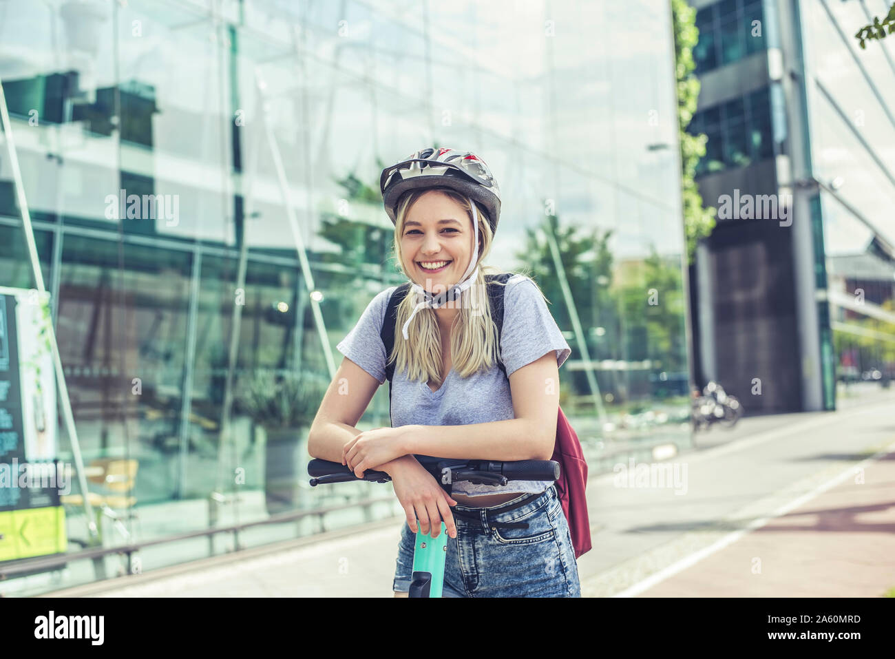 Porträt der glückliche junge Frau mit Radhelm lehnte sich auf Lenker von E-Scooter Stockfoto