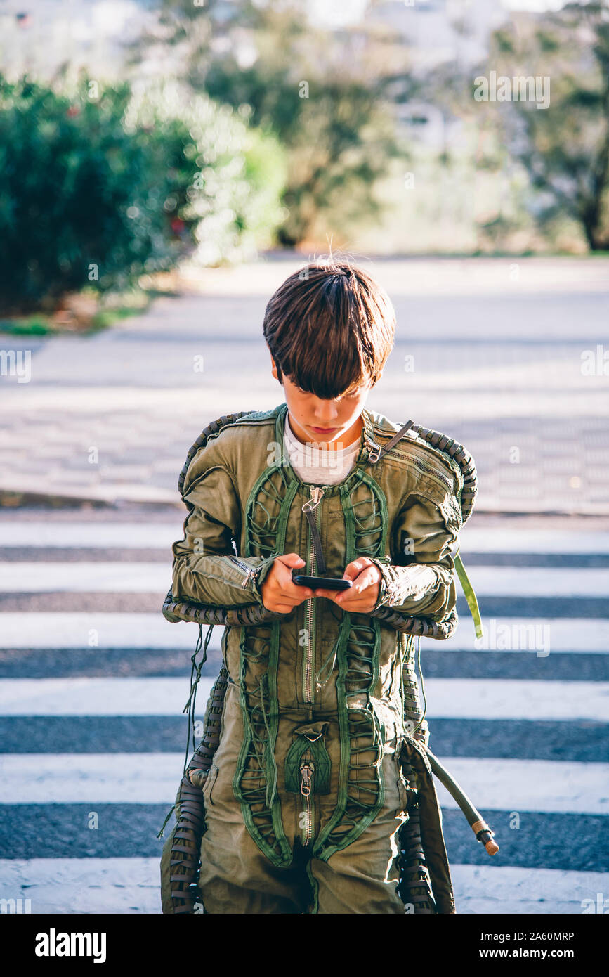 Junge trägt einen Raumanzug, Überquerung der Straße und Sie ihr Smartphone Stockfoto