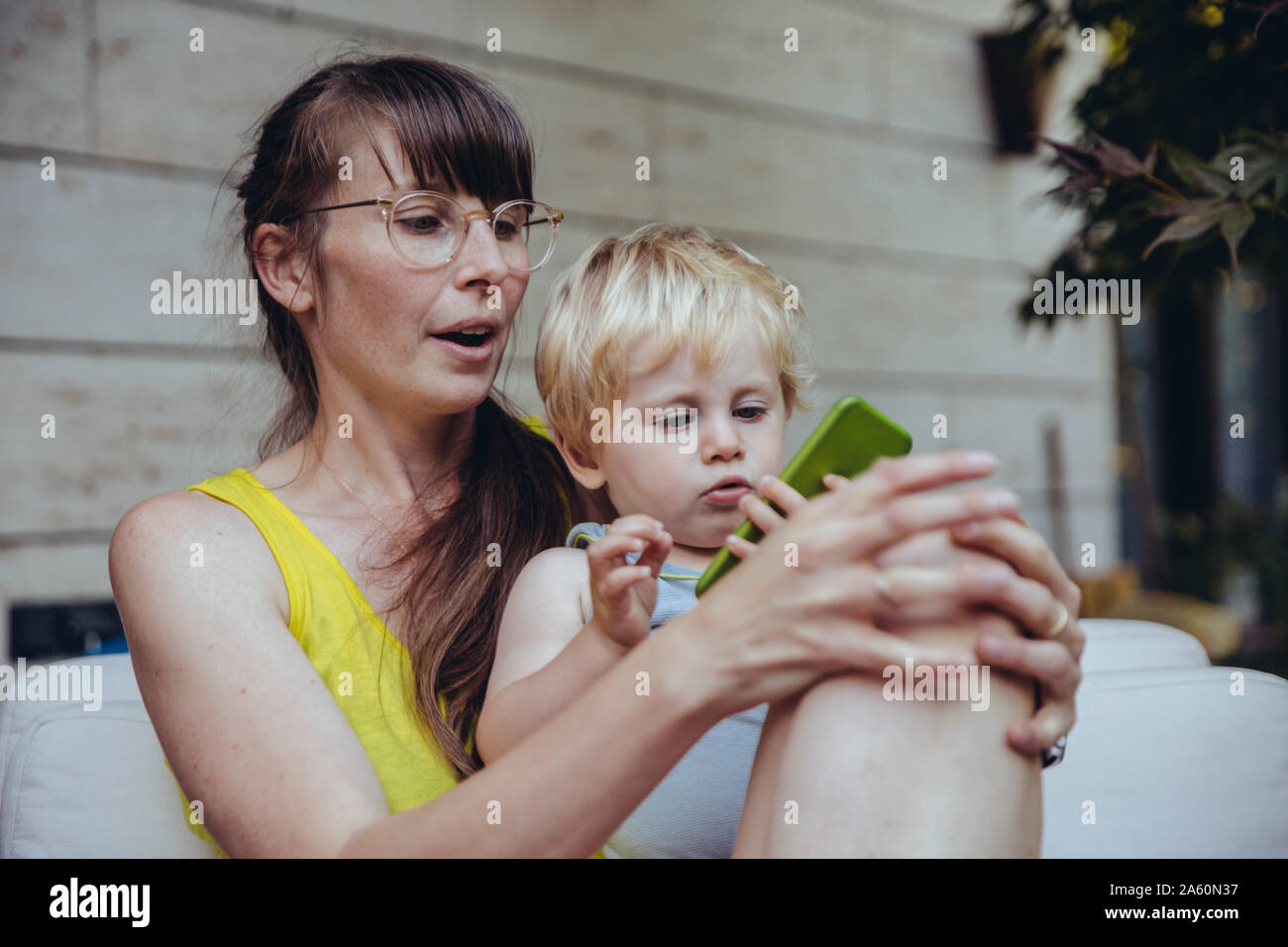 Kleiner Junge sitzt auf dem Schoß der Mutter, an Smartphone suchen Stockfoto