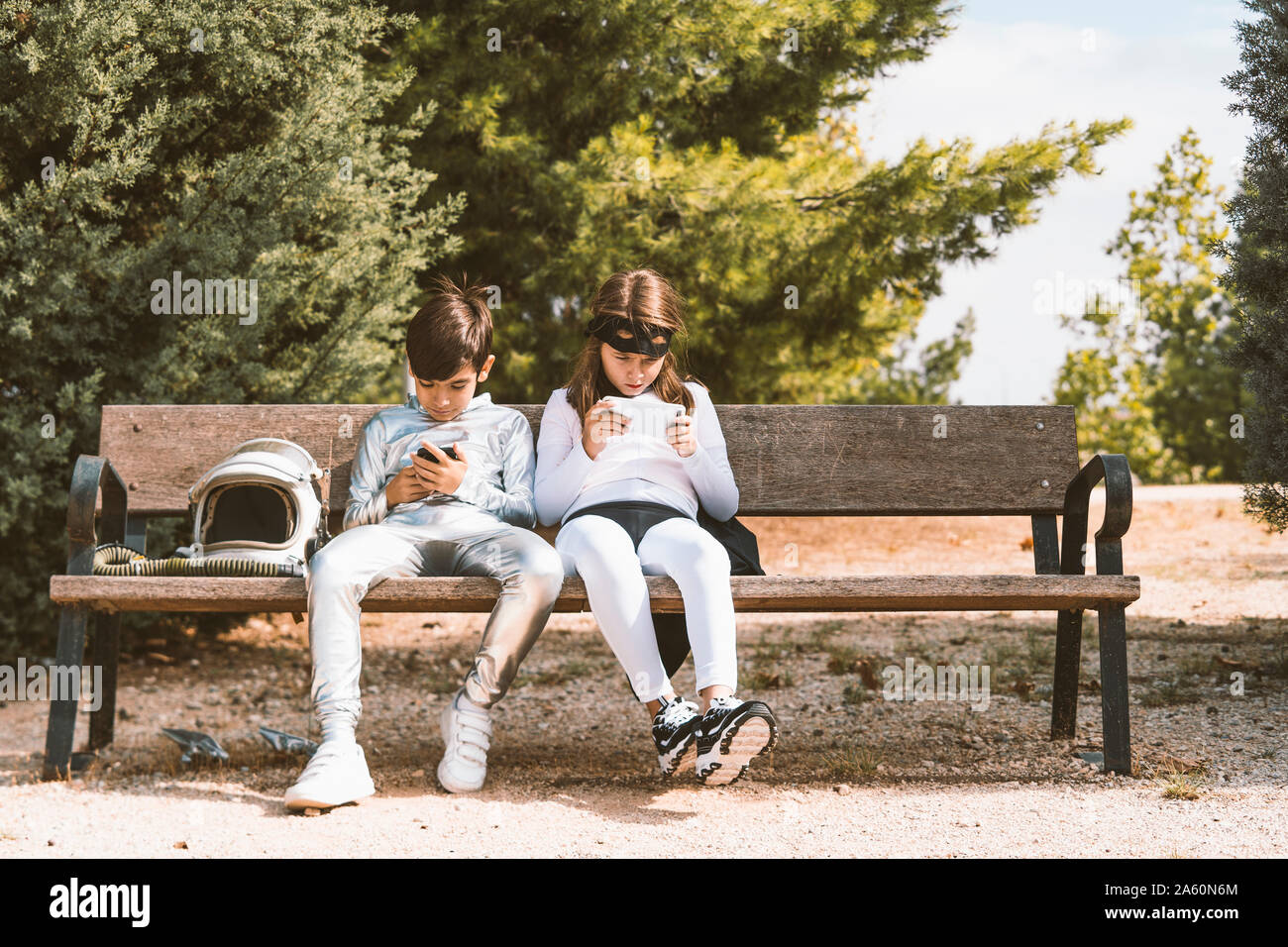 Zwei Zicklein in der Astronaut und Superhelden Kostüme mit Handy auf Parkbank Stockfoto