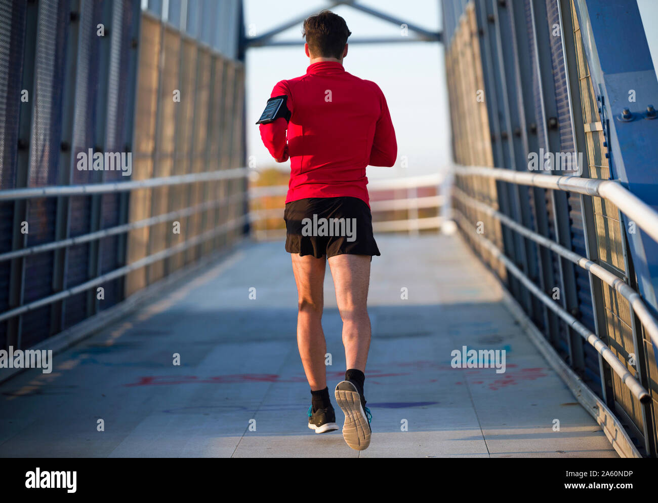 Ansicht der Rückseite ein Jogger mit Smartphone im Arm pocket läuft auf einer Brücke Stockfoto