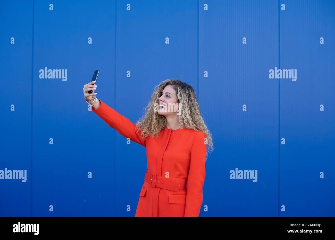 Lächelnden jungen Frau das Tragen der roten Kleid unter selfie vor blauem Hintergrund Stockfoto