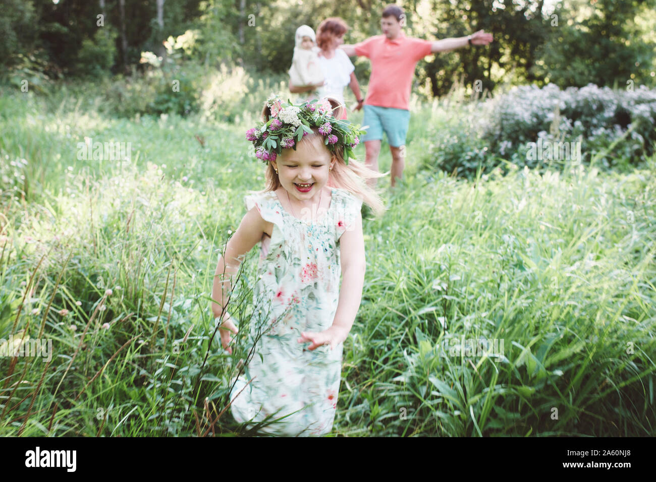 Glückliche kleine Mädchen mit Blume Kranz, die von ihren Eltern in der Natur Stockfoto