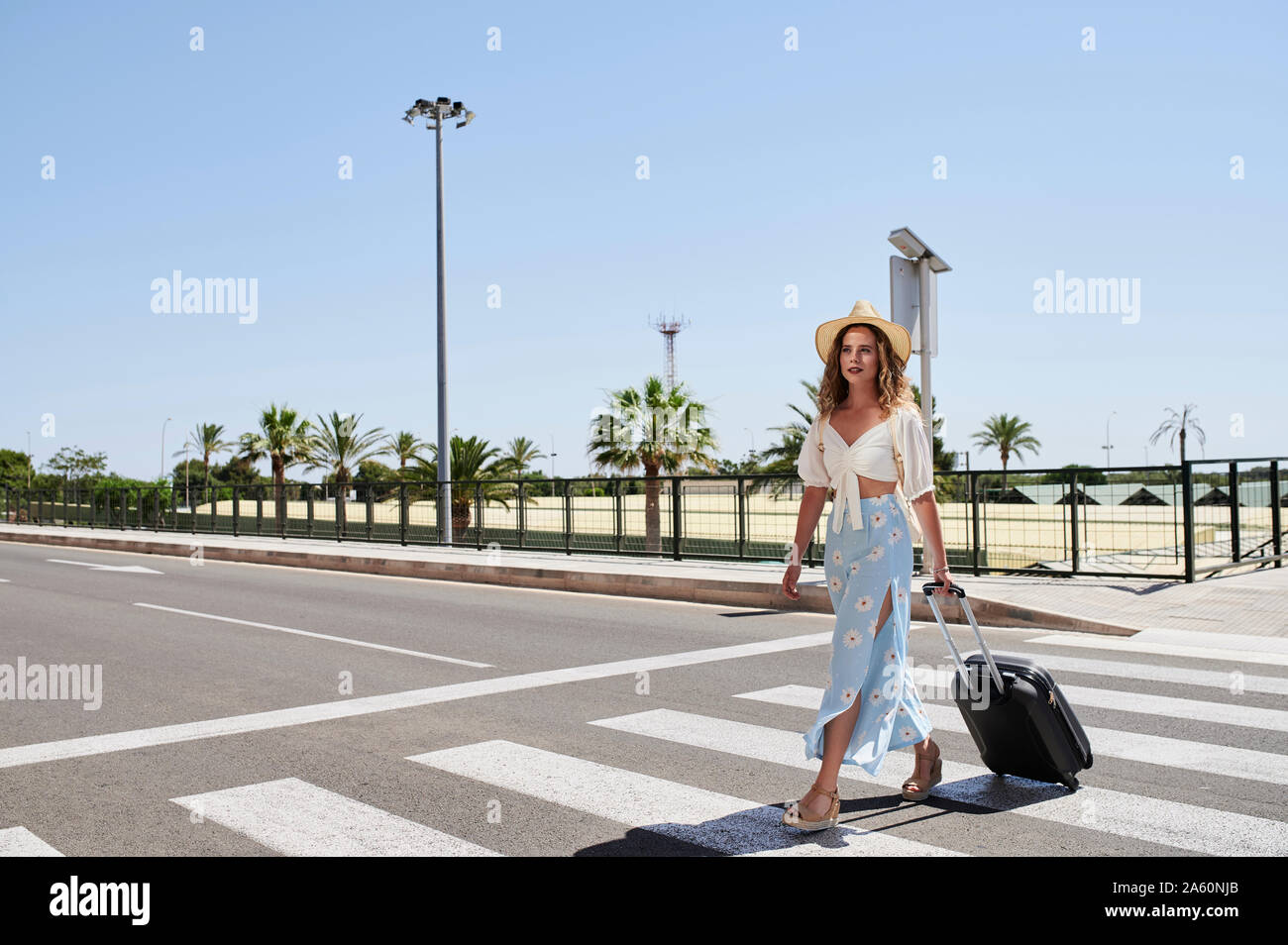 Junge Frau mit Gepäck überqueren einer Straße am Flughafen Stockfoto