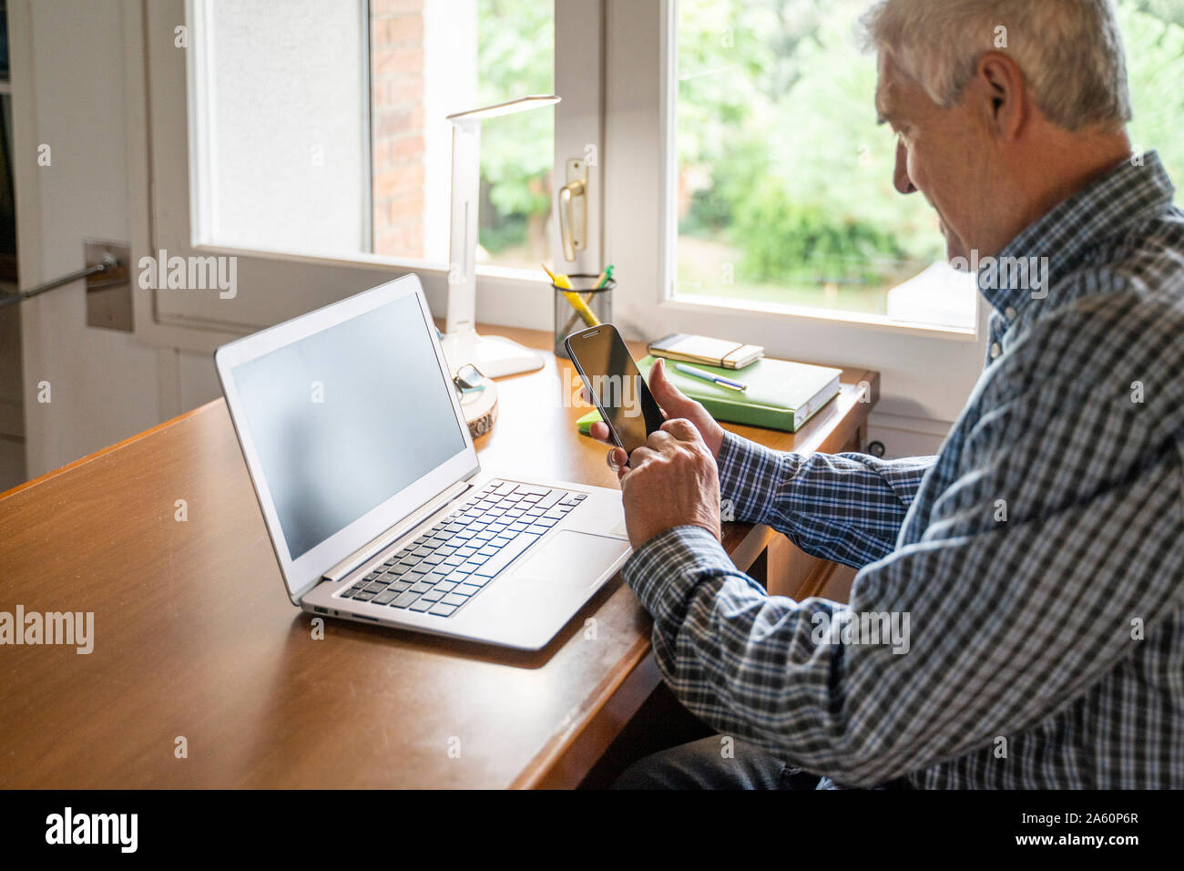 Älterer Mann vor Laptop mit Smartphone zu Hause sitzen Stockfoto