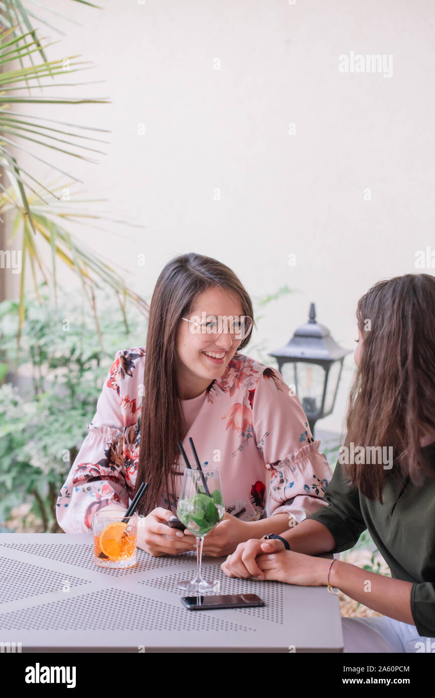 Zwei glückliche junge Frauen am Tisch sitzen mit Cocktails Stockfoto