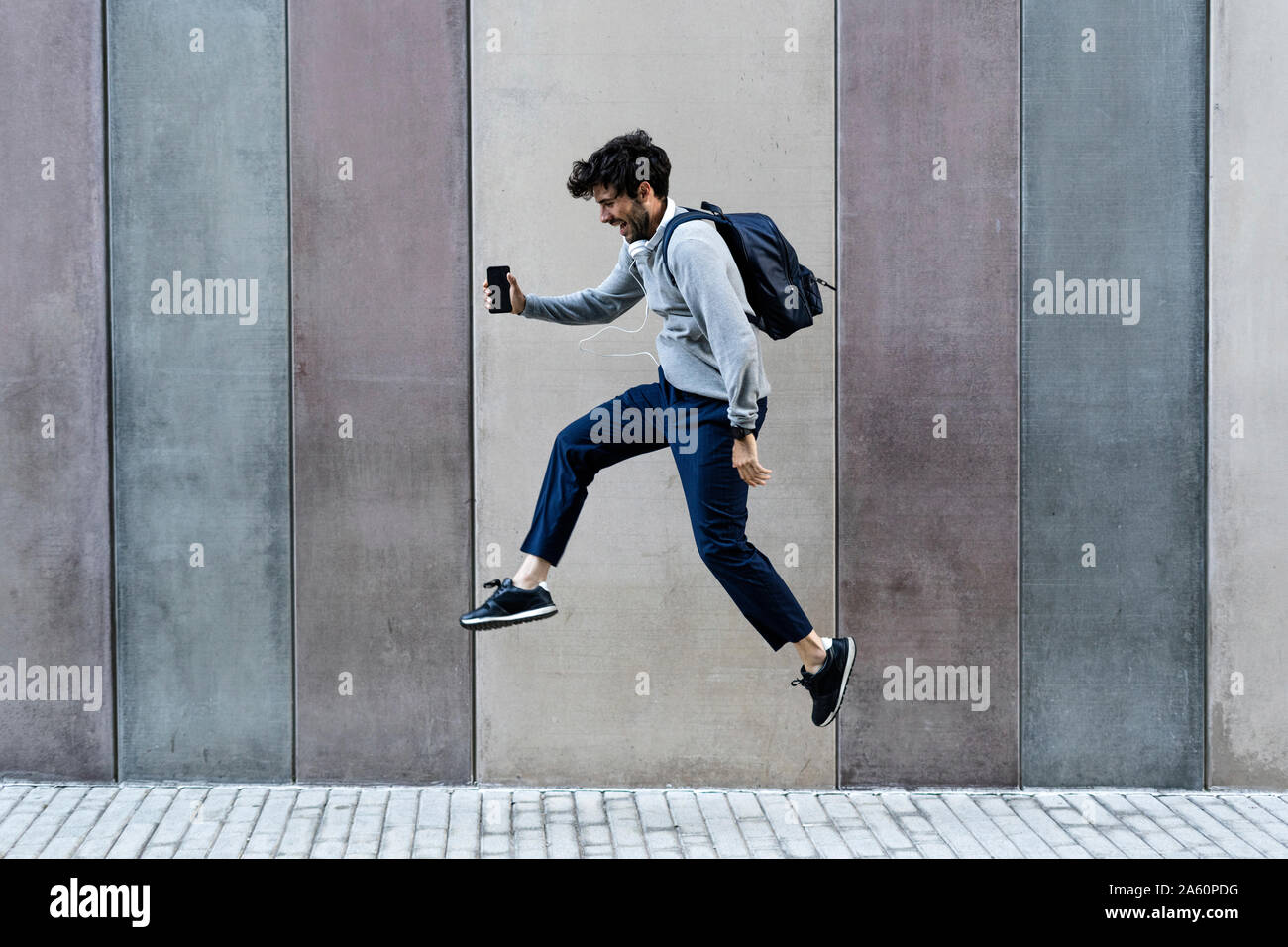 Glücklich Mann mit Handy vor einer Wand springen Stockfoto