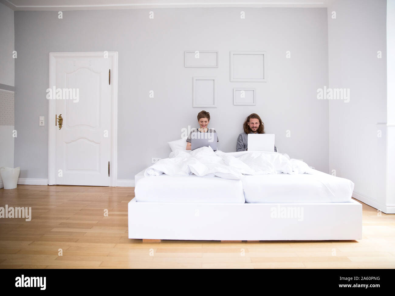 Junges Paar mit Laptops im Bett zu Hause. Stockfoto