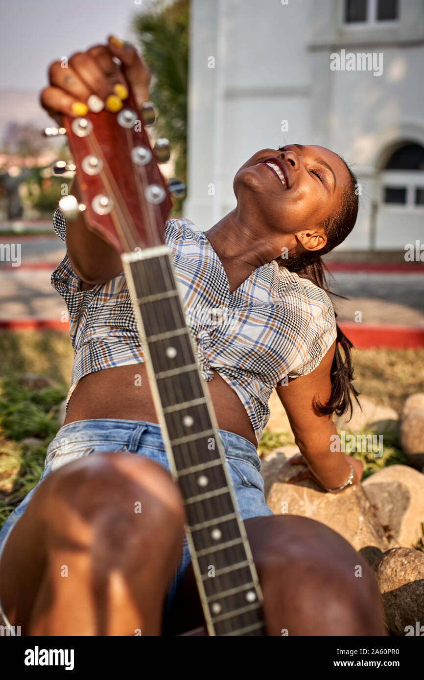 Lächelnde Frau mit Gitarre Sitzen im Freien Stockfoto