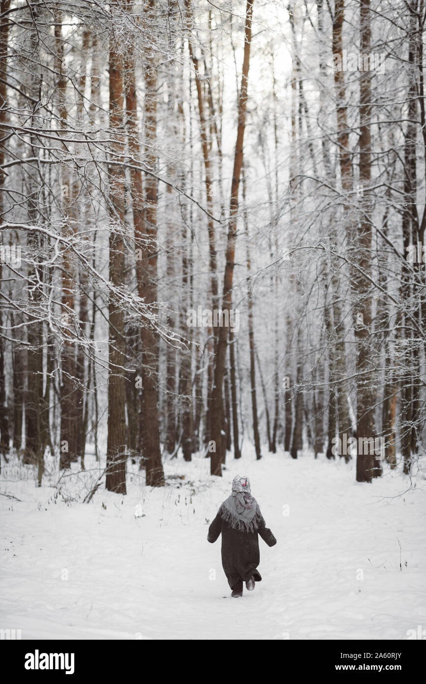 Zurück Blick auf kleine Mädchen mit Kopftuch Walking im Winter Wald Stockfoto
