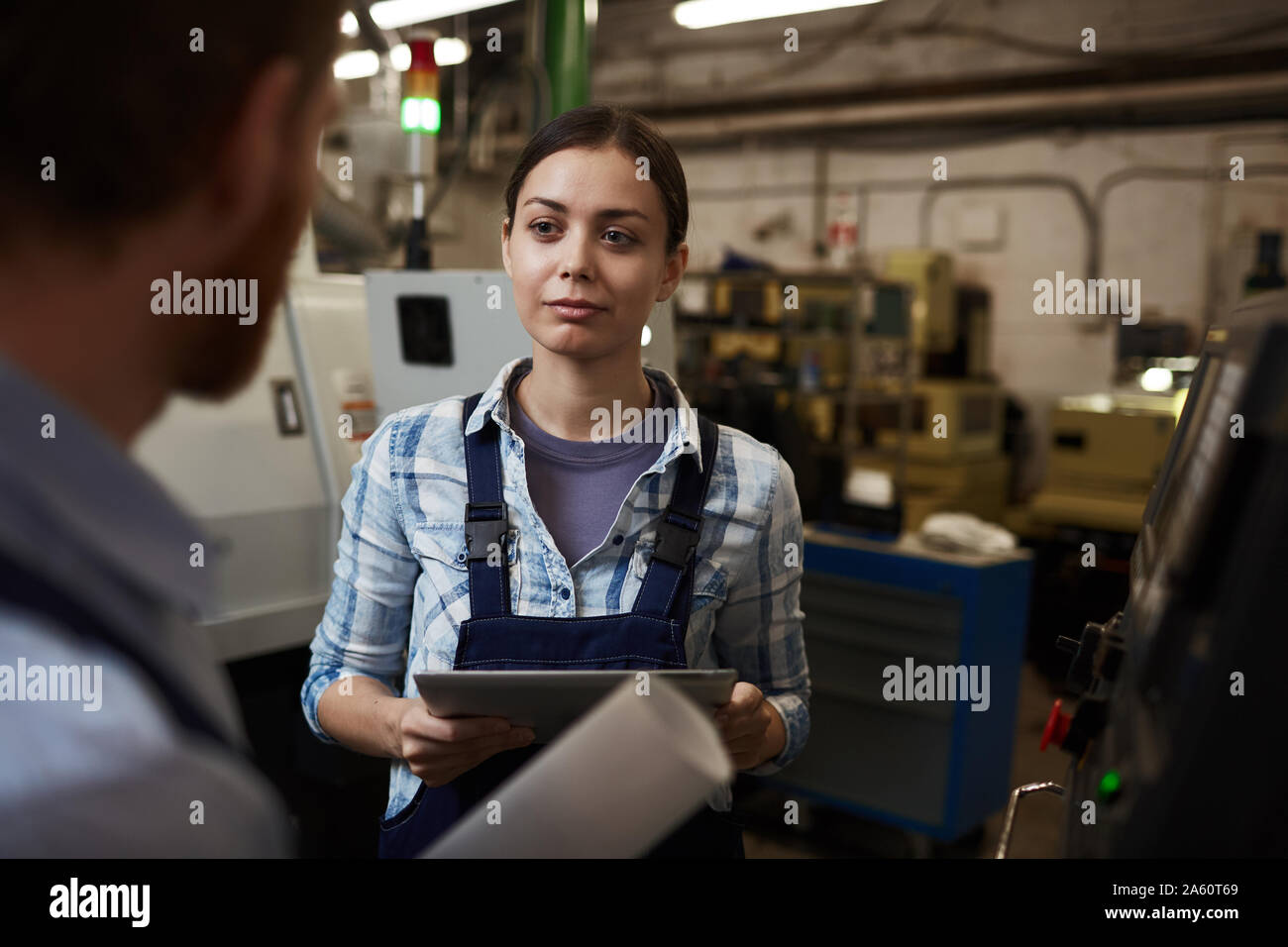 Junge Geschäftsfrau in speziellen Arbeit tragen Holding digital Tablet und das Gespräch mit dem Arbeiter während seiner Arbeiten in der Anlage Stockfoto