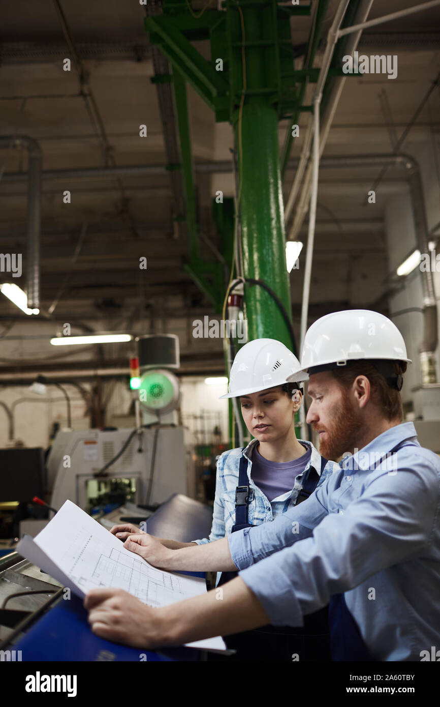 Zwei Ingenieure in speziellen Arbeit tragen und in hardhats bei Blueprint suchen und es gemeinsam diskutieren in der Fabrik Stockfoto