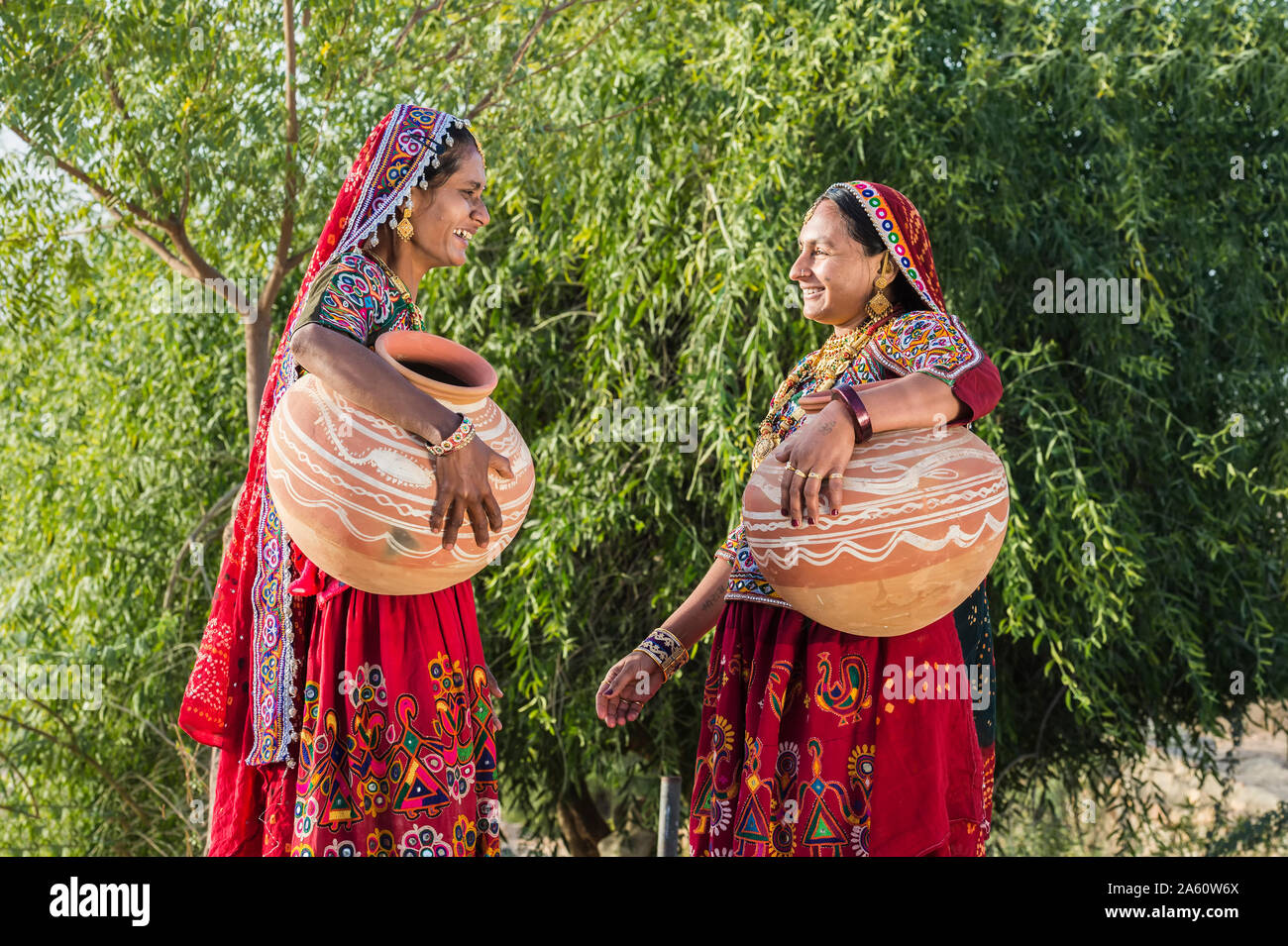 Zwei Ahir Frauen in traditionelle bunte Kleidung tragen von Wasser in einem Ton Kanne, tolle Rann von Kutch Wüste, Gujarat, Indien, Asien Stockfoto