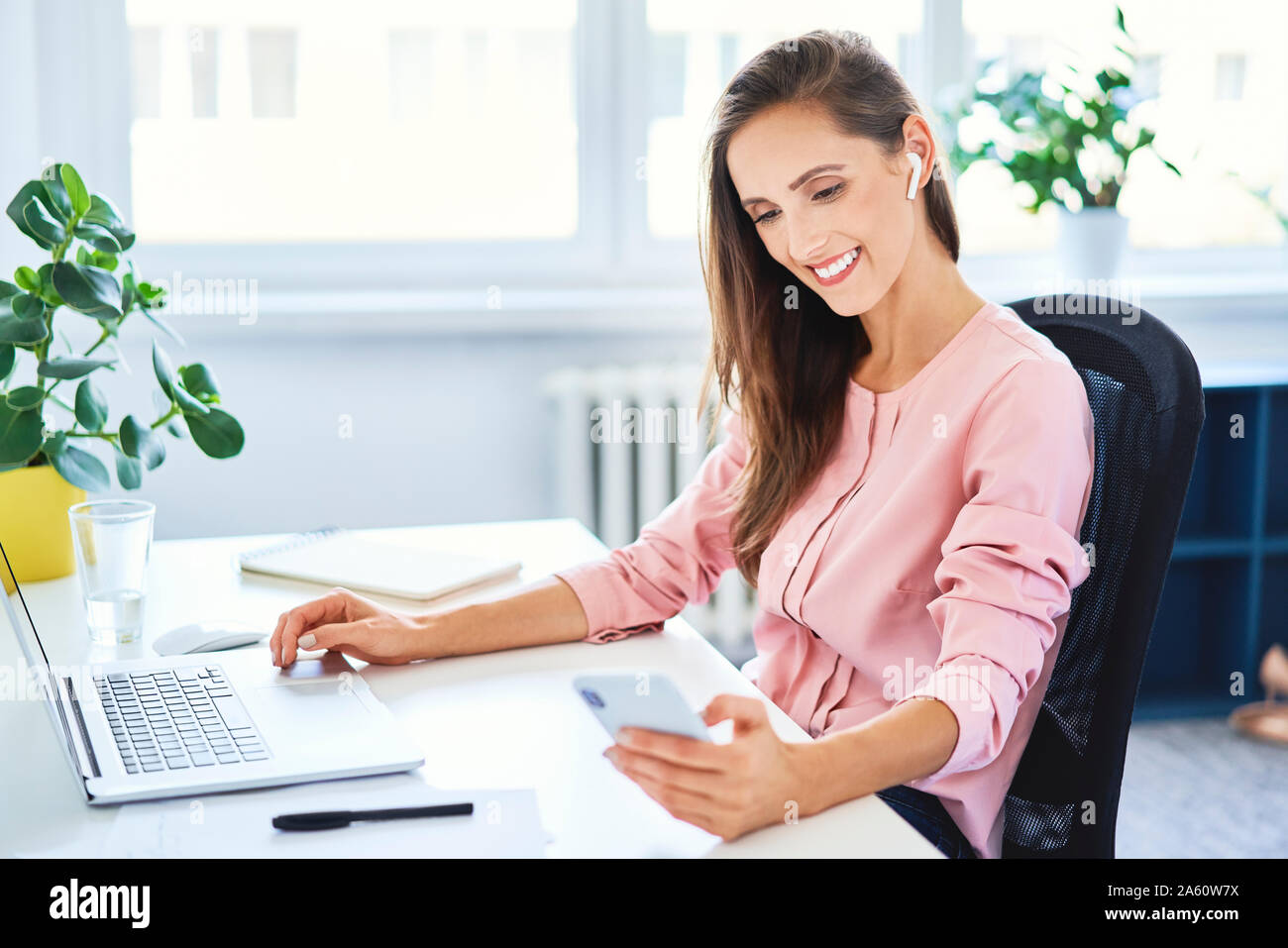 Junge Geschäftsfrau Kontrolle Telefon während der Arbeit am Laptop im Büro Stockfoto