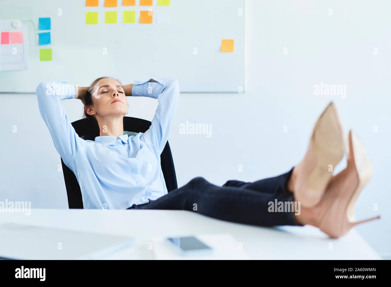 Junge Geschäftsfrau entspannen im Büro liegend mit den Füßen auf dem Schreibtisch Stockfoto