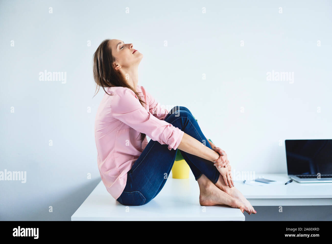 Junge Frau sitzt am Schreibtisch im Büro mit geschlossenen Augen und Entspannend Stockfoto