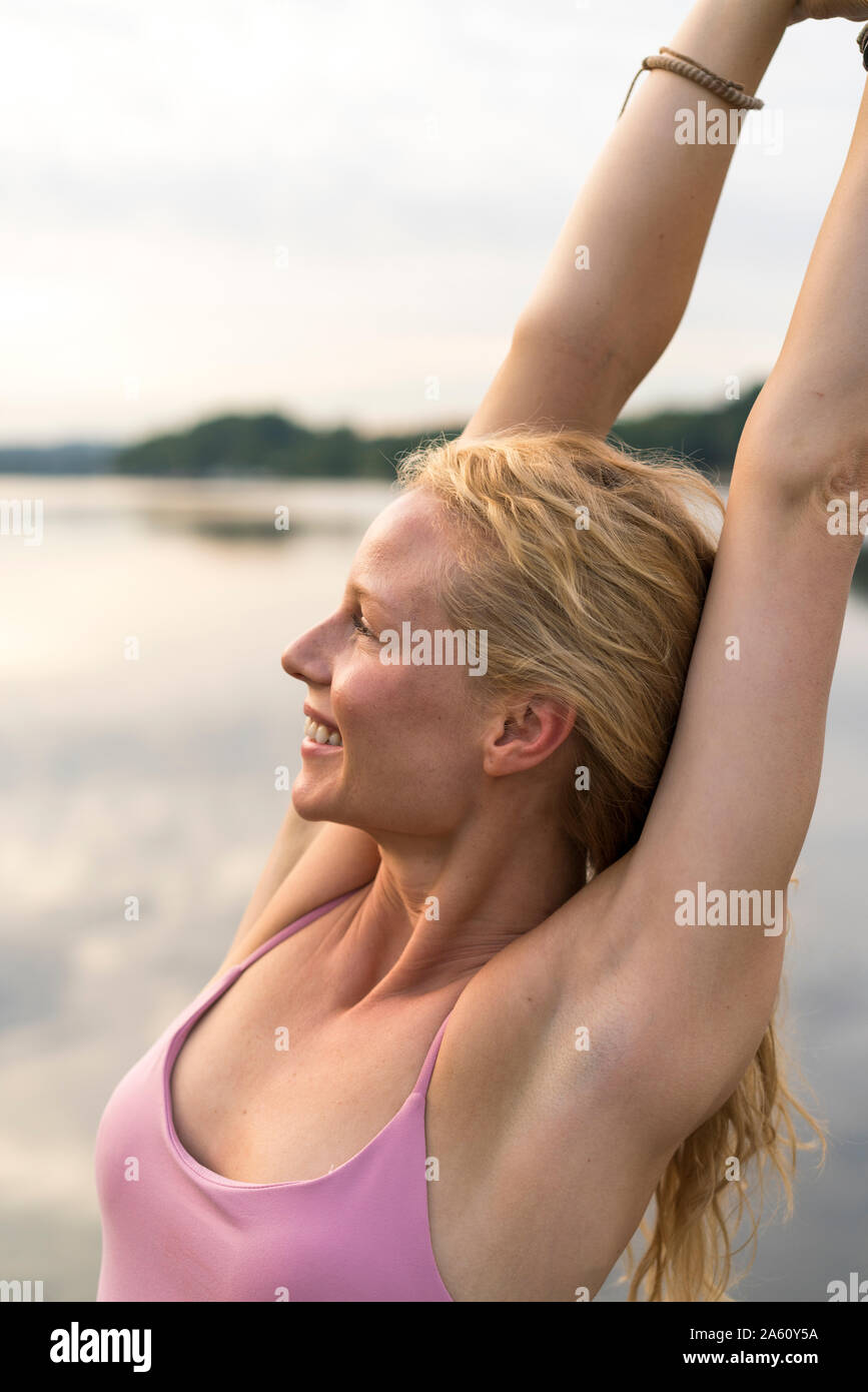 Glückliche junge Frau, die ihre Arme sich heben an einem See Stockfoto