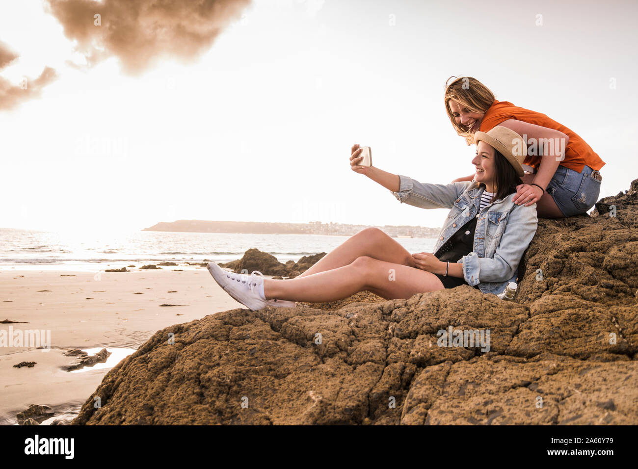 Zwei Freundinnen sitzen auf felsigen Strand, wobei Smartphone selfies Stockfoto