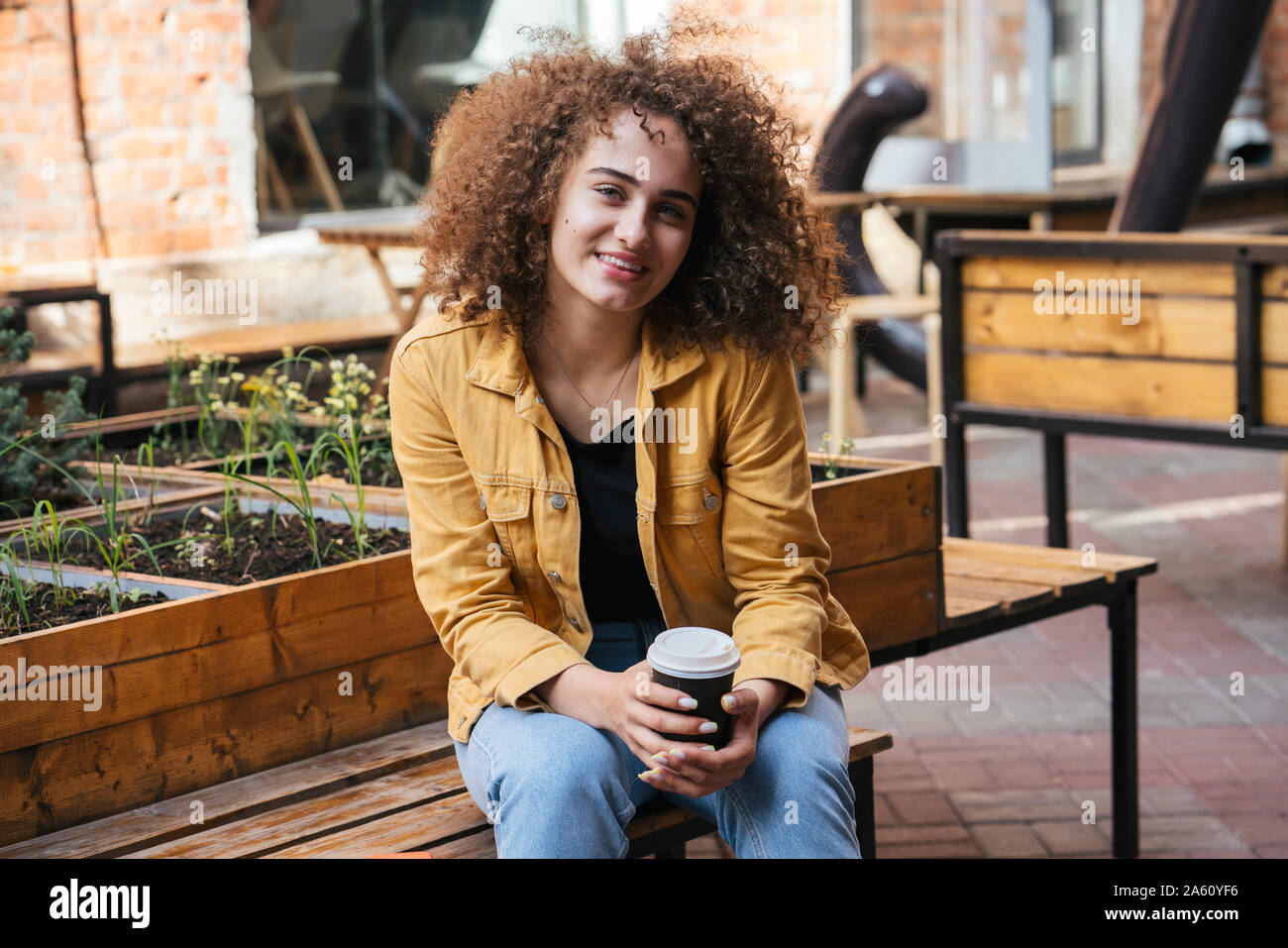 Portrait Of Smiling teenage Mädchen sitzt auf der Bank mit Kaffee zu gehen Stockfoto