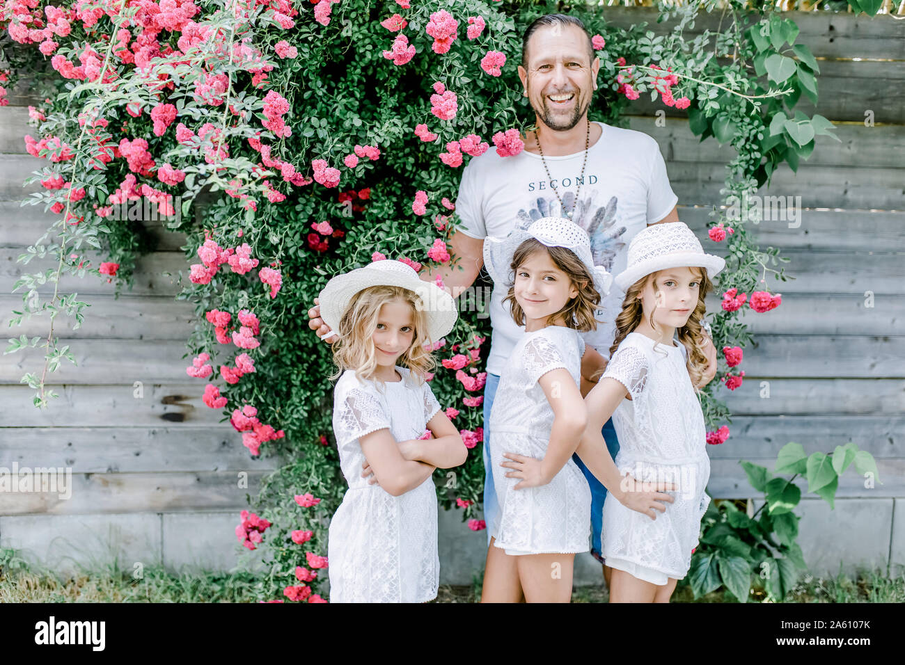 Gerne Vater mit drei Triplet Schwestern posiert an einem Rosenstrauch Stockfoto