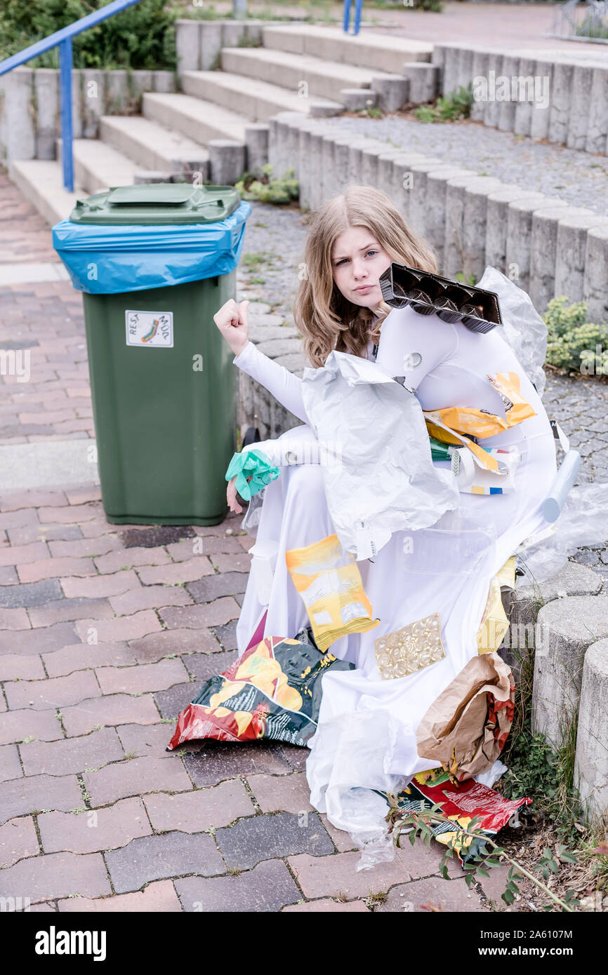 Teenager tragen weiße Kleid mit Kunststoffabfällen, sitzt neben einem Mülleimer Stockfoto