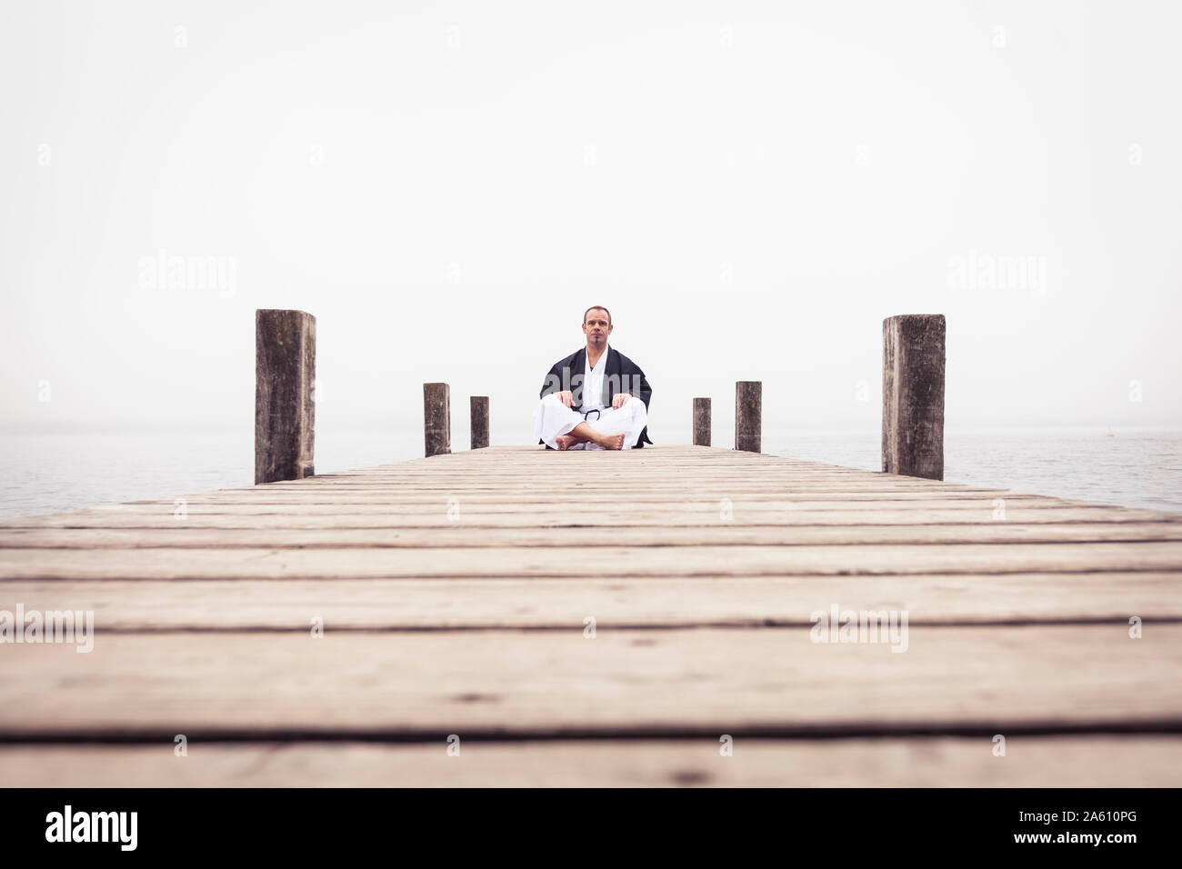 Mann sitzt auf Steg Yoga Übung, Starnberger See, Deutschland Stockfoto