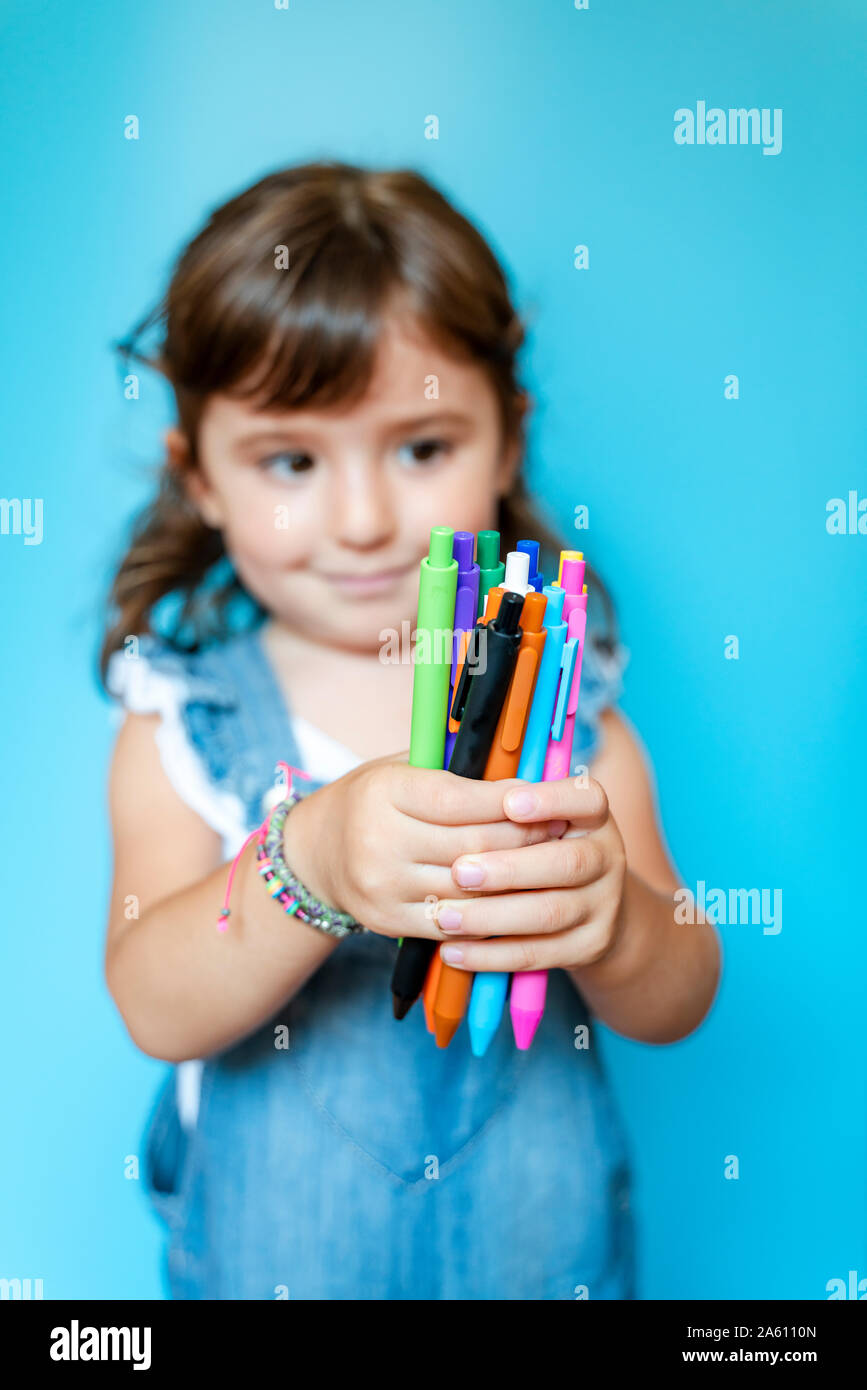Portrait von niedlichen kleinen Mädchen herauf eine Handvoll farbige Kugelschreiber auf blauem Hintergrund Stockfoto