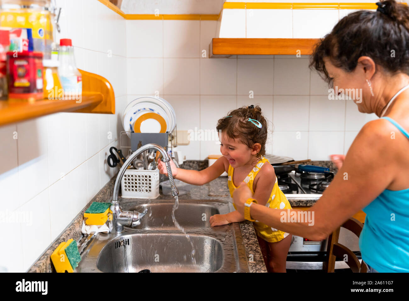 Kleine Mädchen und Großmutter spielen mit Wasser in der Küche Stockfoto