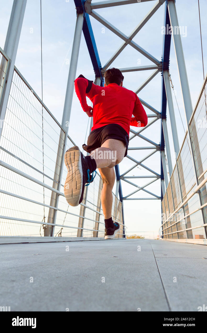 Jogger mit Smartphone im Arm pocket läuft auf einer Brücke Stockfoto