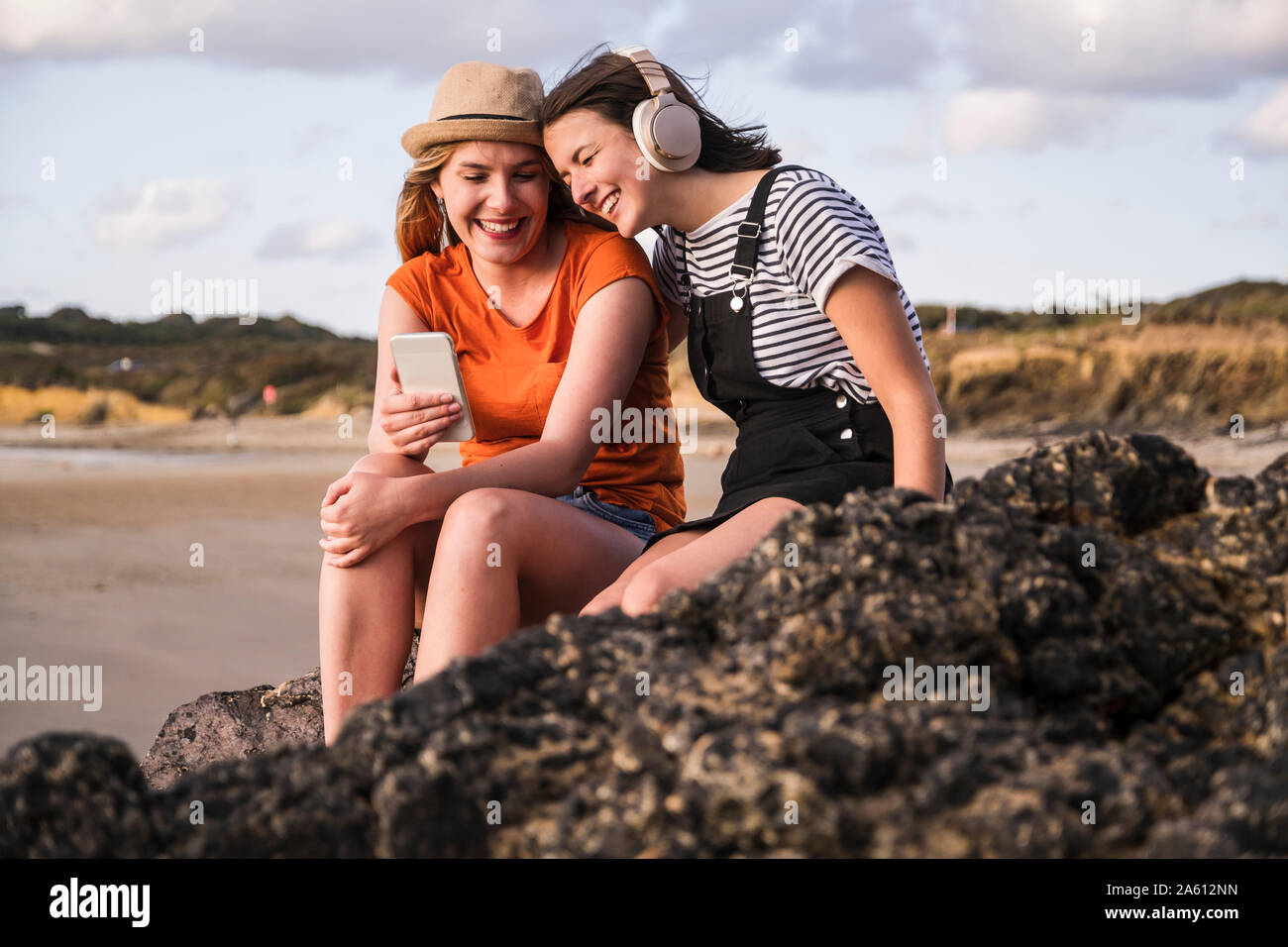 Zwei Freundinnen sitzen auf felsigen Strand, mit Smartphone, Zuhören miusic Stockfoto