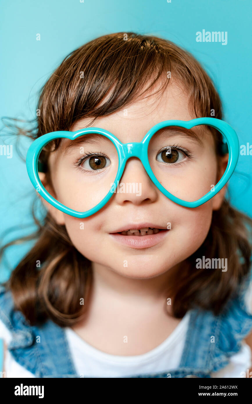 Portrait von niedlichen kleinen Mädchen mit Herz geformte Gläser auf blauem Hintergrund Stockfoto