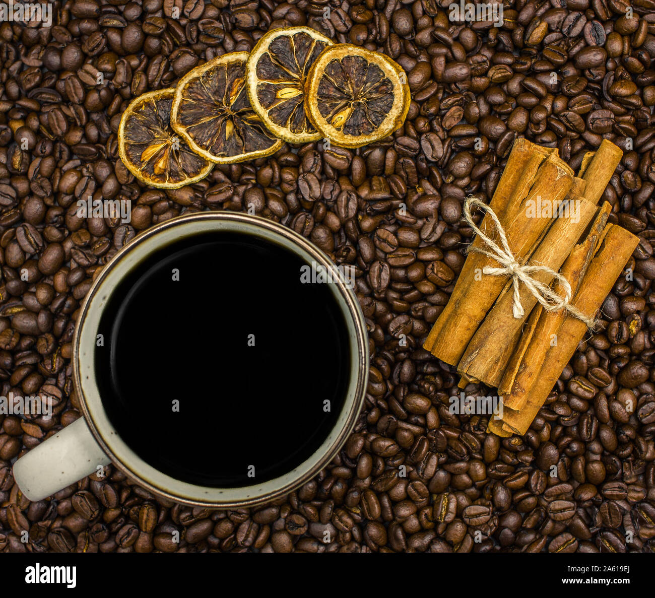 Blick von oben auf eine Tasse schwarzen Kaffee, Zimtstangen und getrockneten Orangenscheiben auf einem Bett von Kaffeebohnen Stockfoto